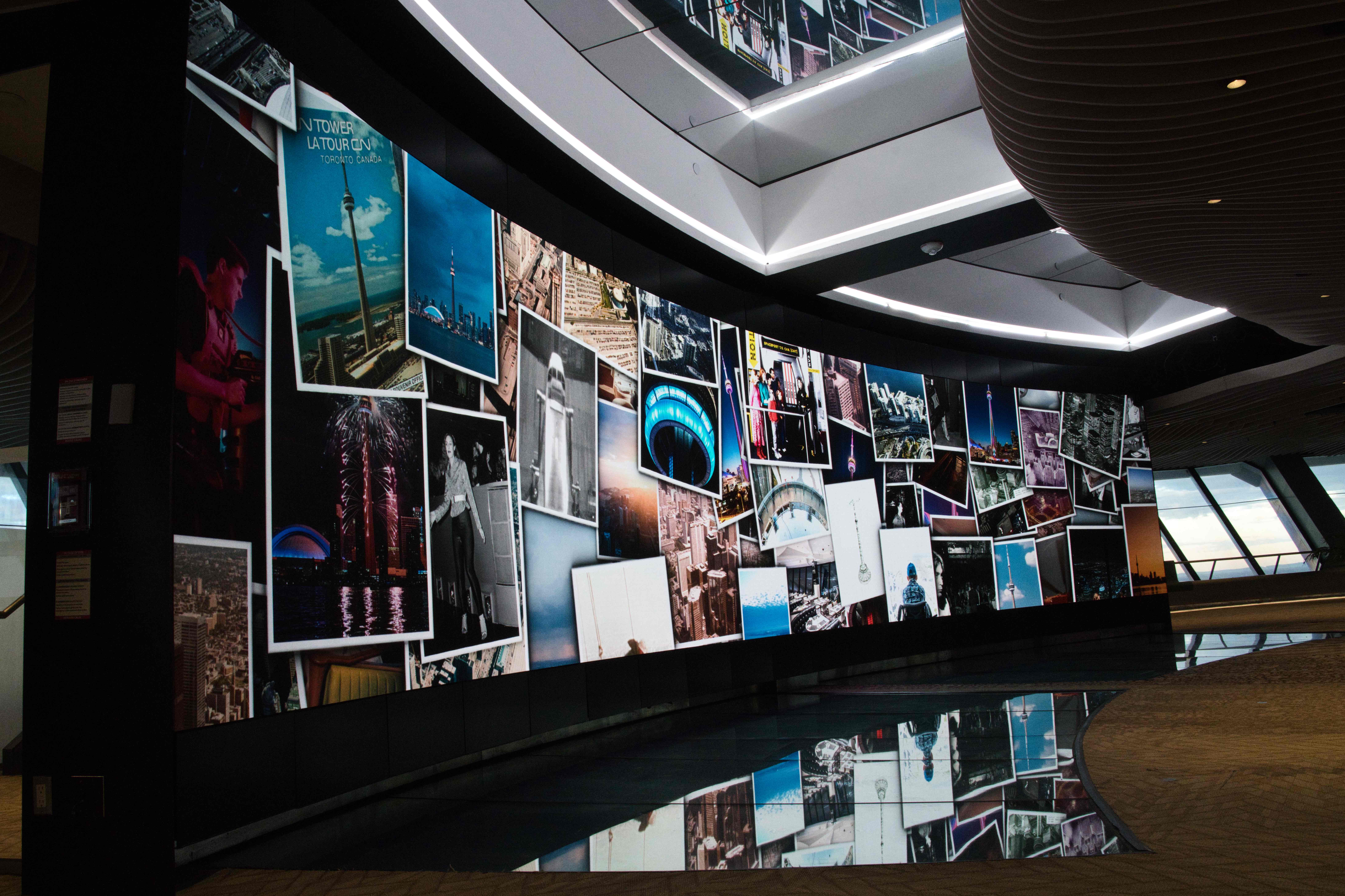 Curved video wall on the CN Tower's Lower Observation Level showing a collage of CN Tower photos, reflected in the floor