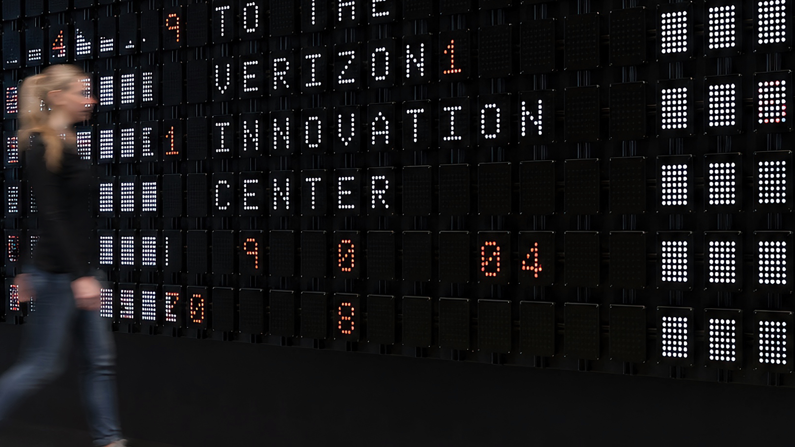 A visitor walks past the wall as Verizon Innovation Center appears in white dot-matrix letters among red digits