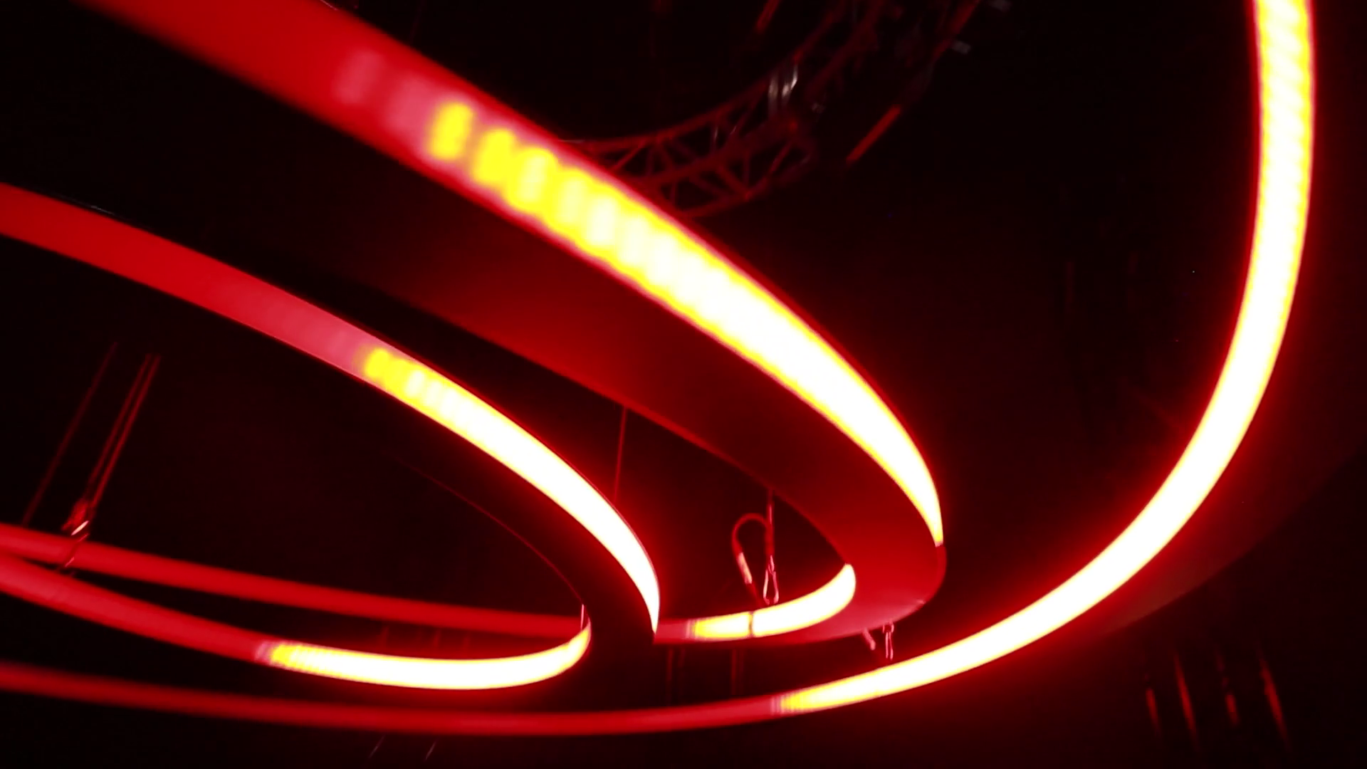 Looking up at the chandelier's red-lit rings sweeping overhead, with the rigging truss above