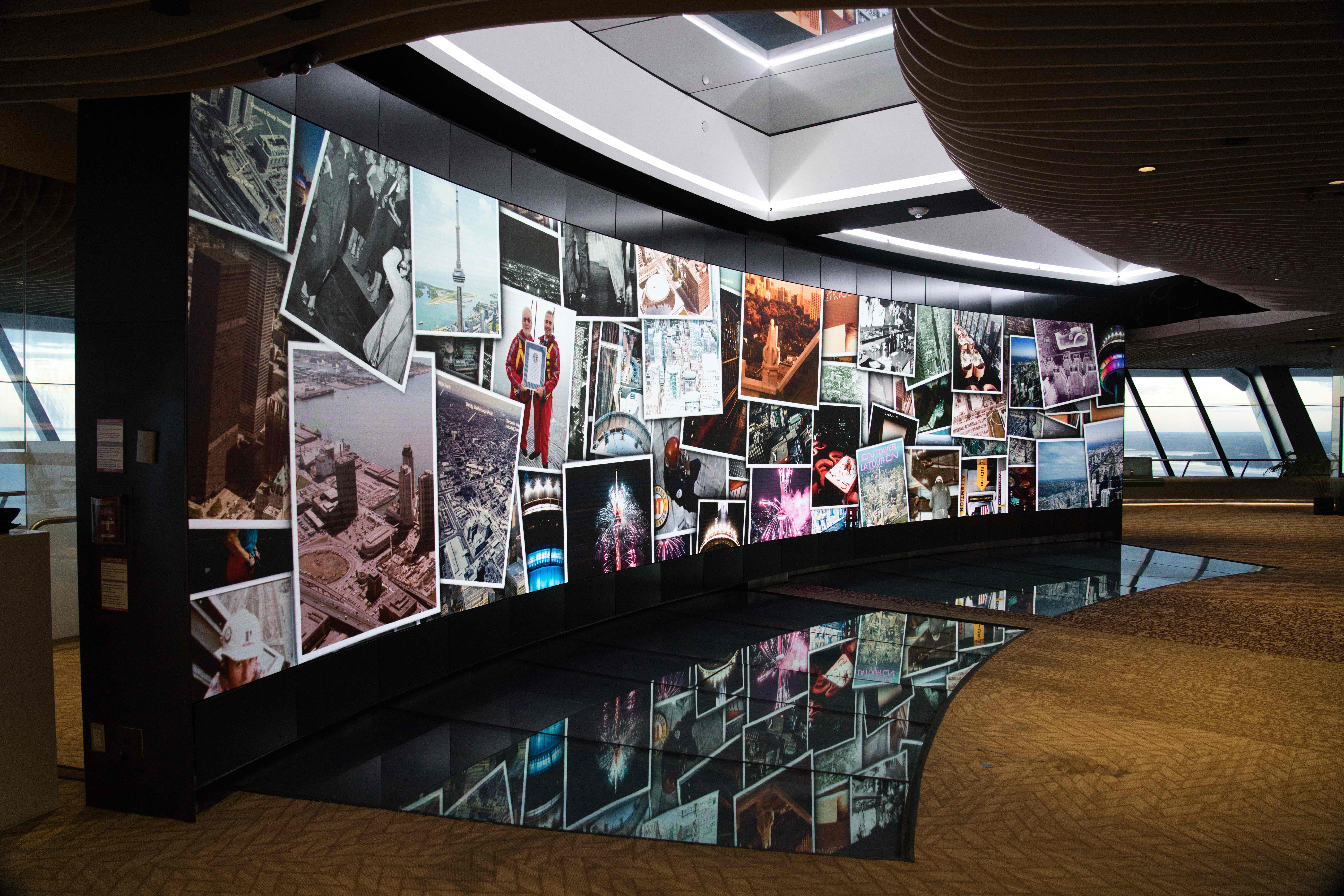Wide view of the curved video wall showing a collage of archival CN Tower photos, mirrored in the dark floor