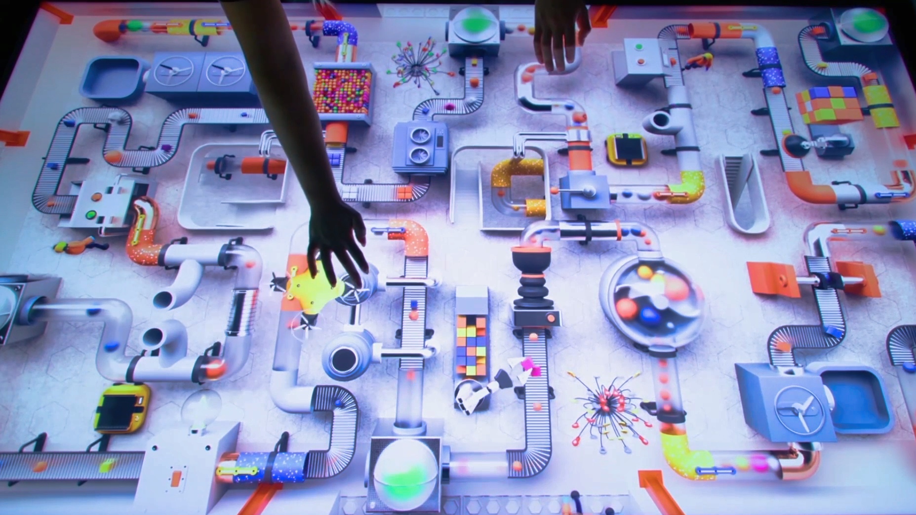 Hands reach across the Smart Factory interactive table, an illustrated top-down factory of conveyors and machines