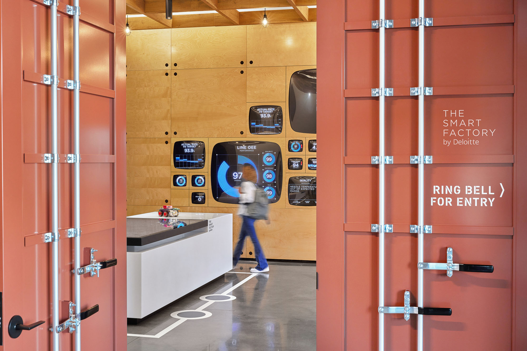 Container doors marked The Smart Factory by Deloitte open onto the interactive table and a wall of live gauges