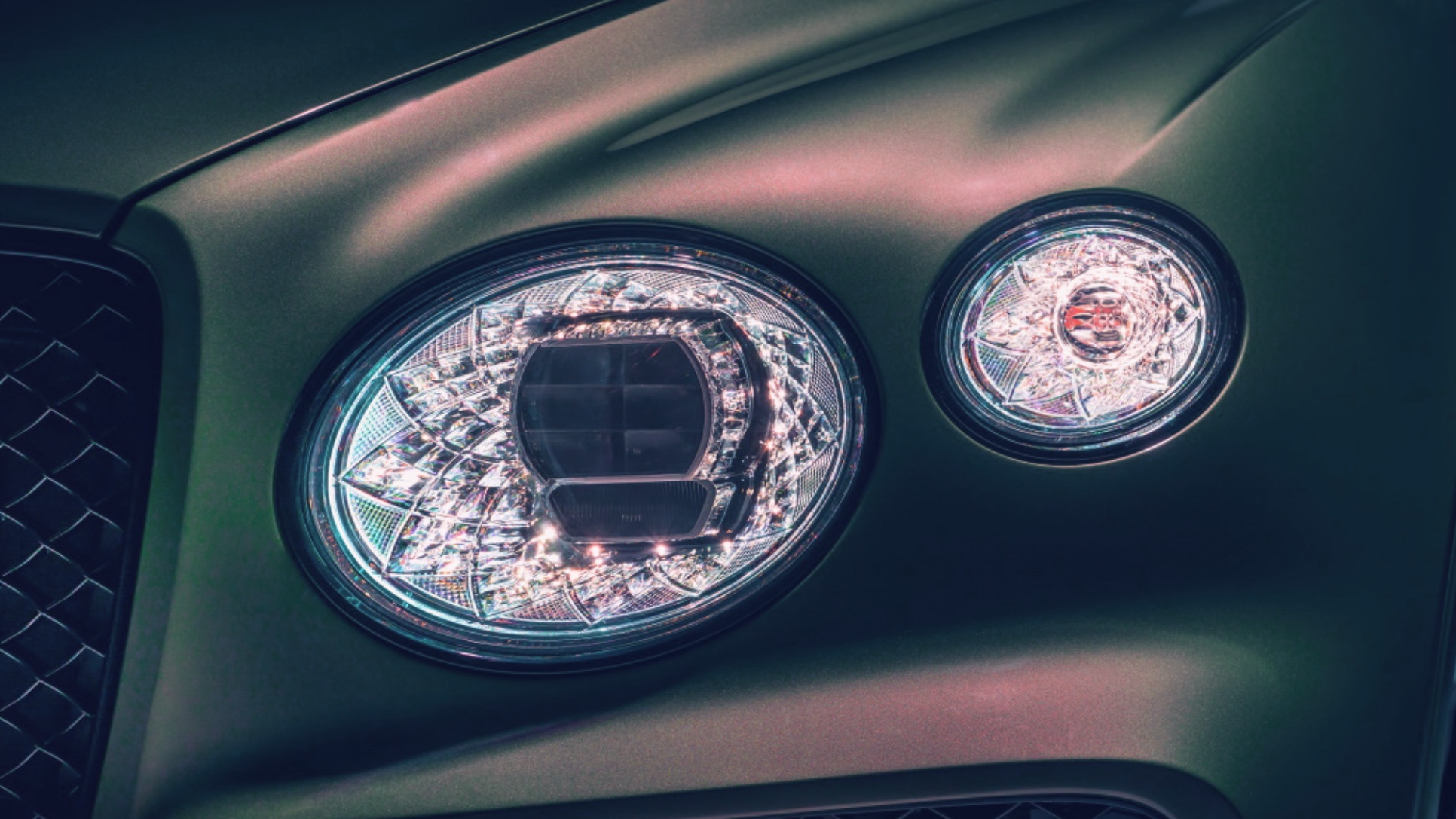 Illuminated Bentley headlamps with faceted, jewel-like detailing set in dark green paintwork