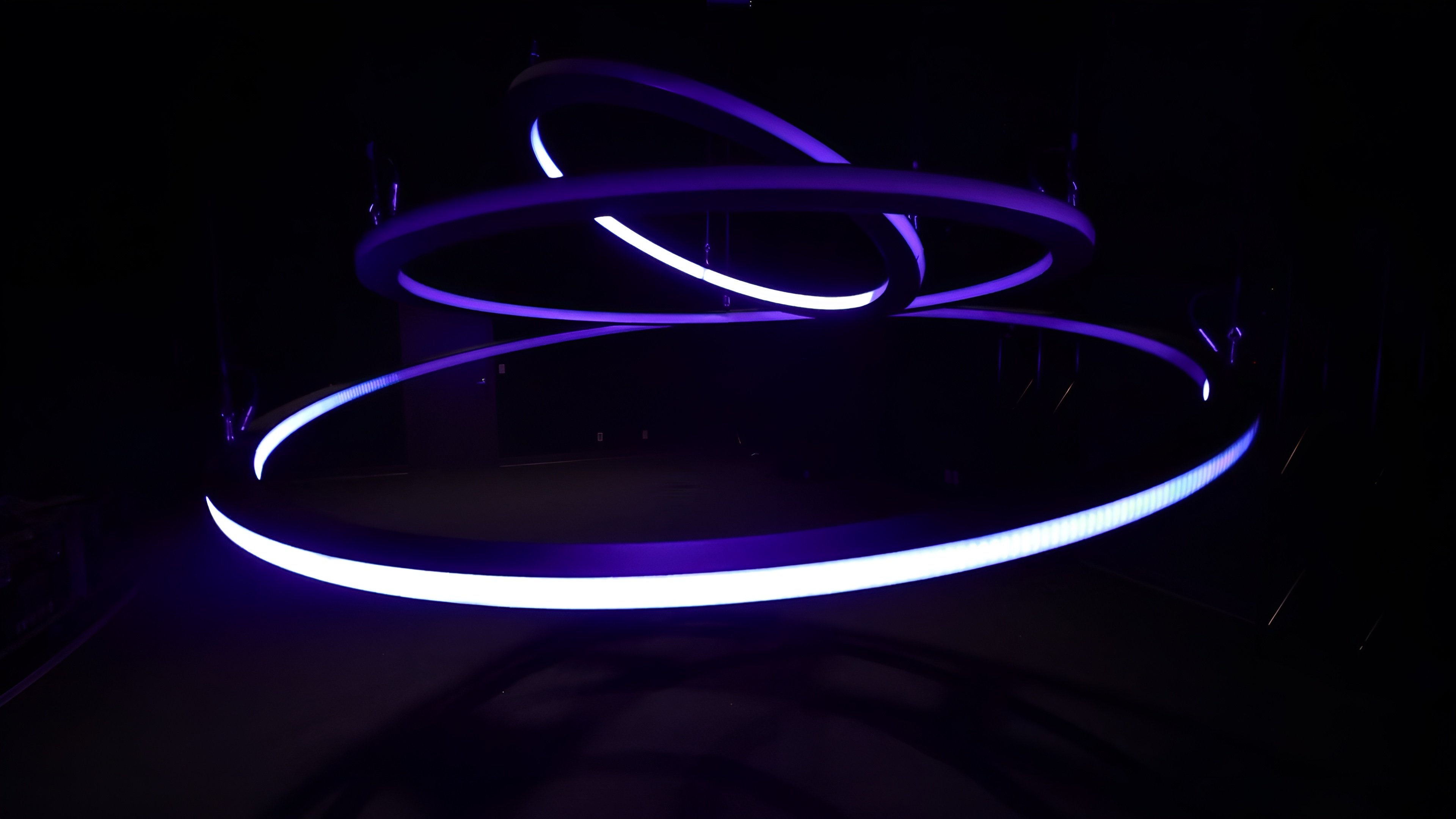 The three concentric rings of the kinetic chandelier lit violet, tilted at different angles in a dark room